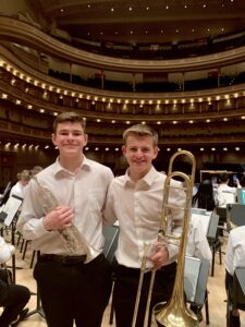 two teens in suits with musical instruments in a concert hall.