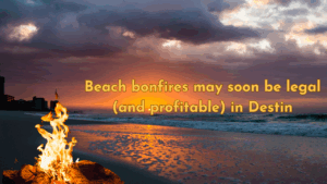A beach bonfire burns in the foreground at sunset on a Destin, Florida shoreline, with text overlay reading “Beach bonfires may soon be legal (and profitable) in Destin.”