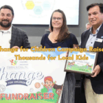 Superintendent presents award to Ruckel Middle School staff for raising the most money in Okaloosa’s Change for Children Campaign, with banner and plaque visible.