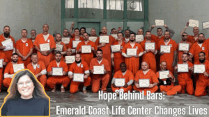 A large group of incarcerated men dressed in orange jumpsuits proudly hold certificates of completion inside a correctional facility. They are graduates of the Anchored Dorm program, run by the Emerald Coast Life Center. In the foreground, a smiling woman is featured in a cutout overlay — Dana Clah, the founder of the program, whose faith-based, trauma-informed approach is transforming rehabilitation in Okaloosa County.