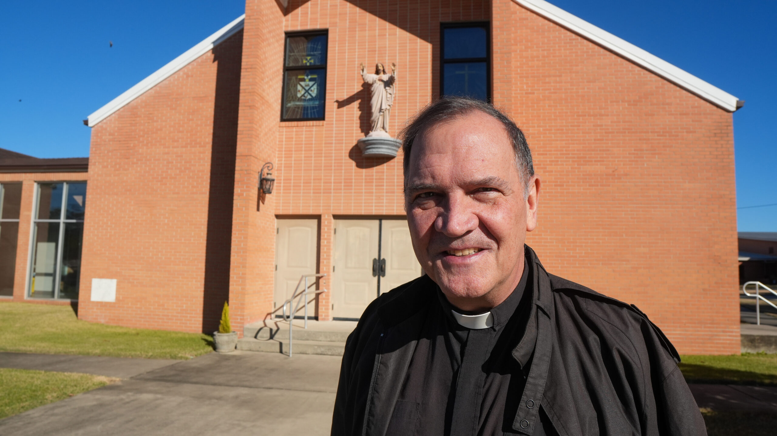 a Catholic priest stands in front of his church.