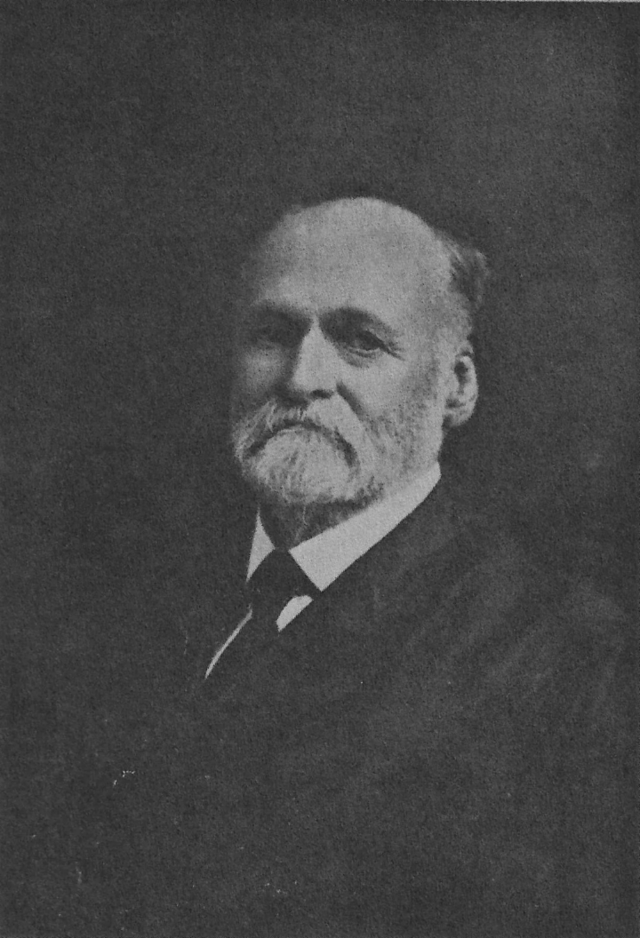 Older man with a white beard in a dark suit and tie, looking slightly to the left.